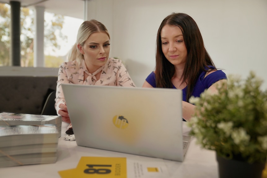 Brisbane-based real estate agent Jett Jones looks at a laptop with a colleague.