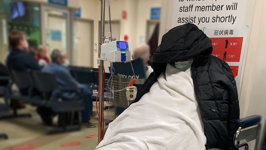 A man on a stretcher in a hospital room with his face obscured
