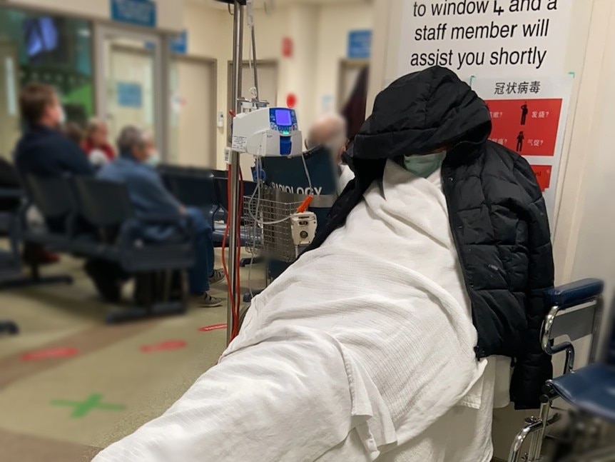 A man on a stretcher in a hospital room with his face obscured