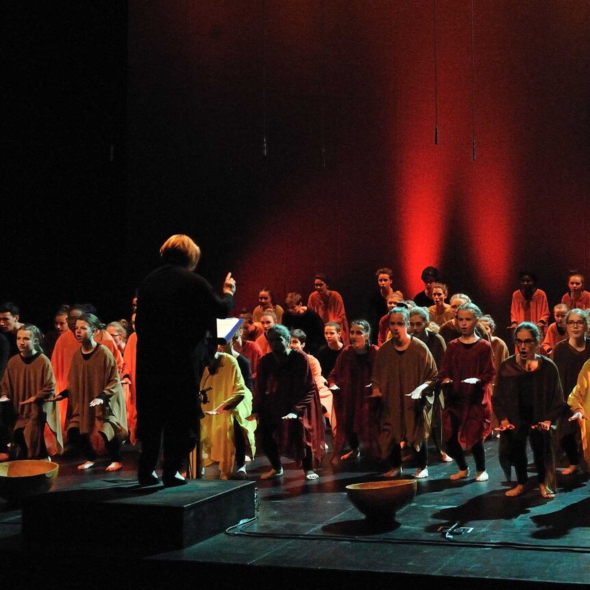 French choir Le Cigale de Lyon wearing orange, red and brown poncho-type robes and crouching down while singing