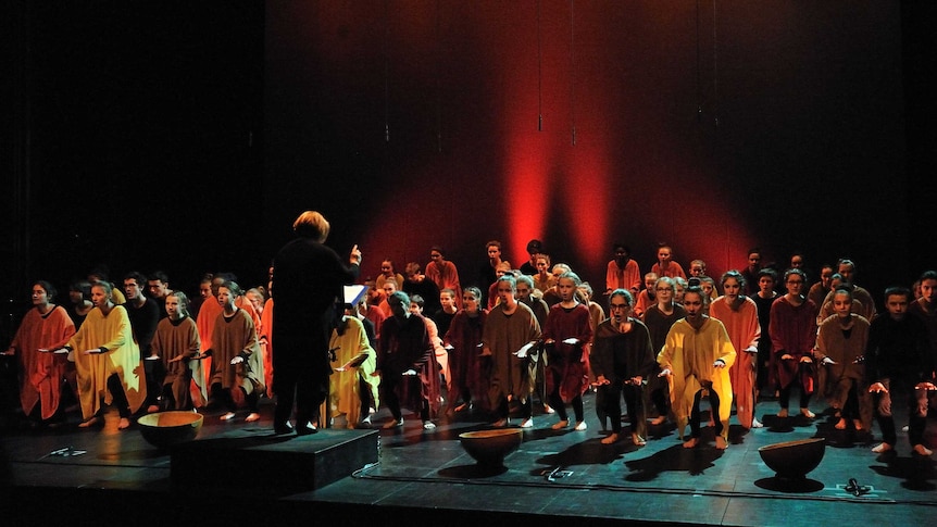 French choir Le Cigale de Lyon wearing orange, red and brown poncho-type robes and crouching down while singing