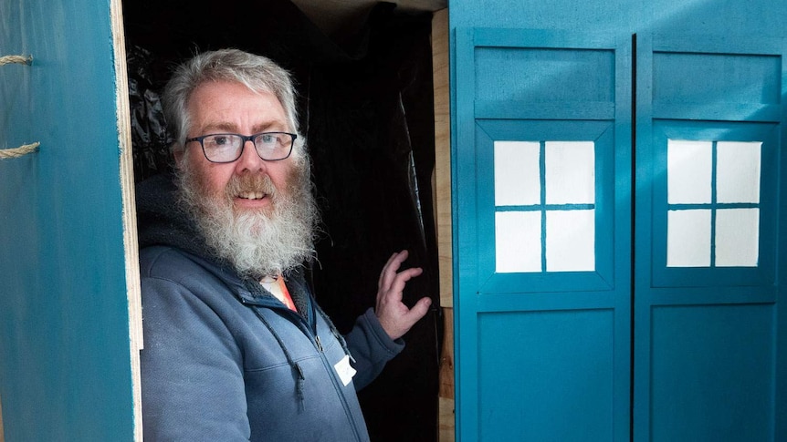 A man stands inside an upright blue coffin built to look like Doctor Who's tardis time machine