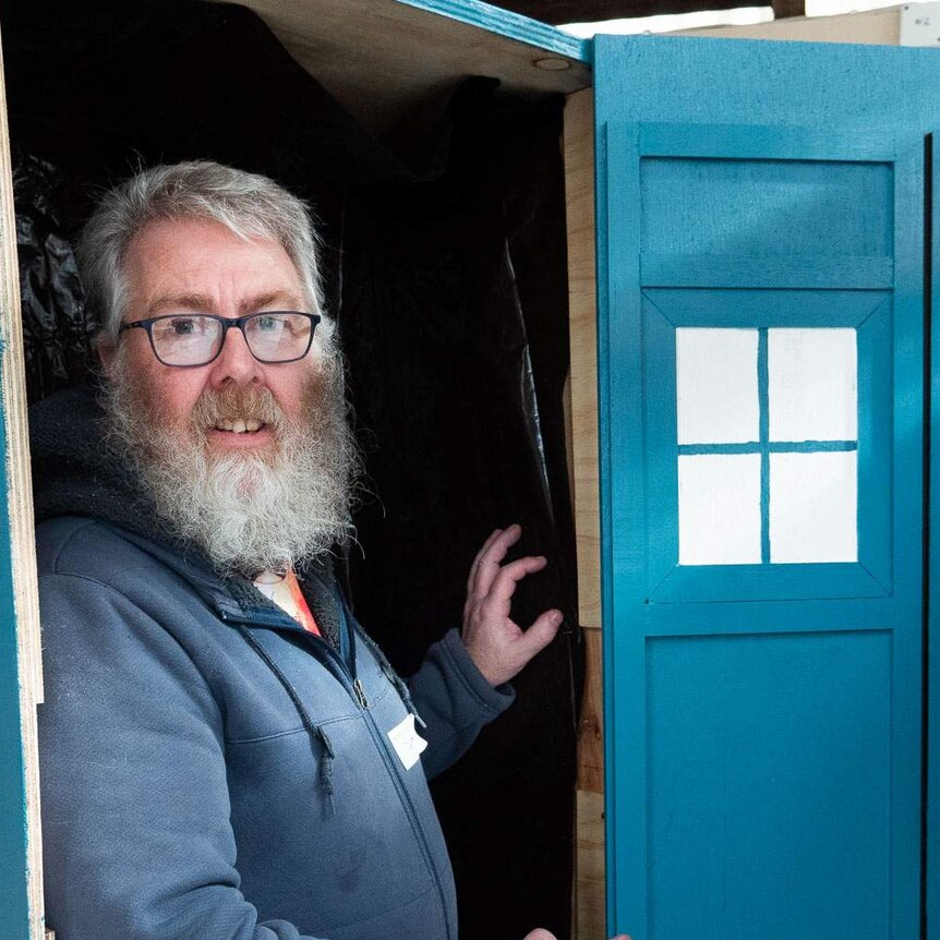 A man stands inside an upright blue coffin built to look like Doctor Who's tardis time machine