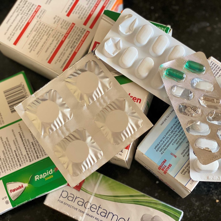 A pile of blister packs and boxes of pills lie on a counter.