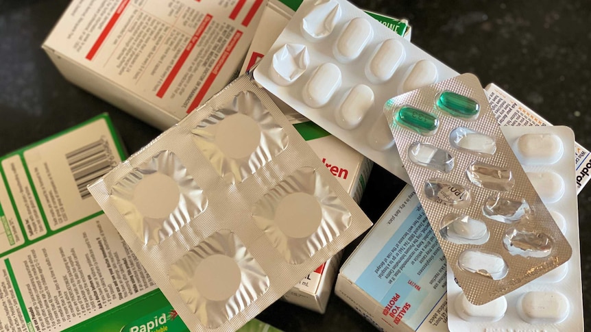 A pile of blister packs and boxes of pills lie on a counter.