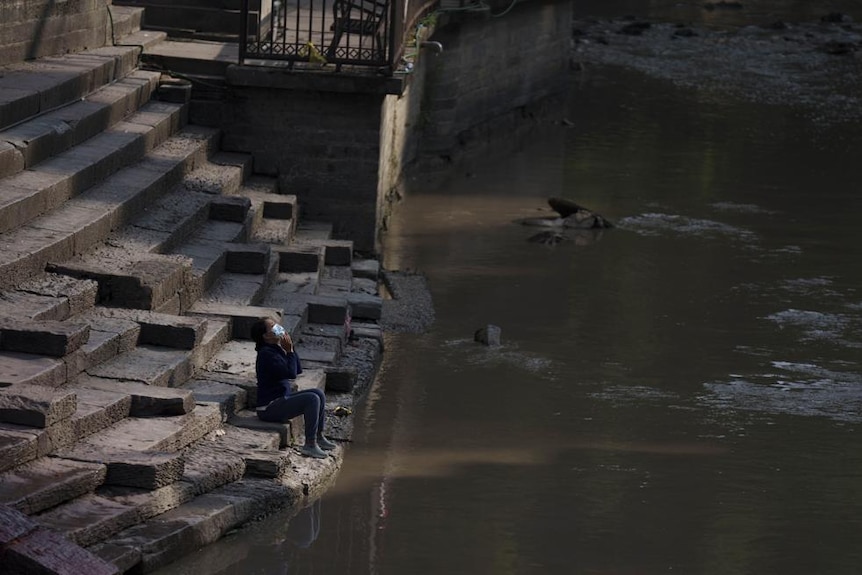 A woman prays on the banks of the brown coloured Bagmati River in Kathmandu