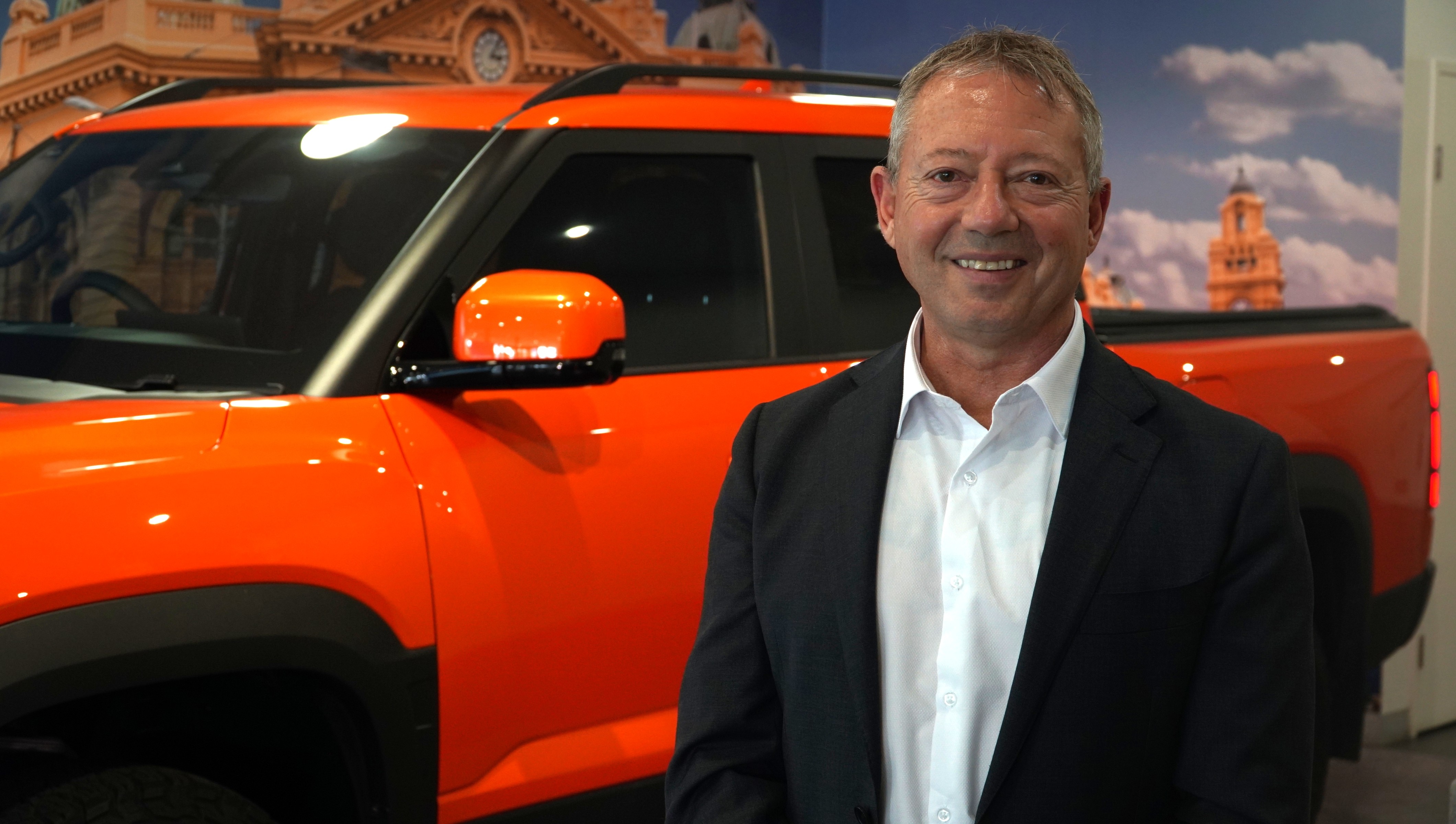 A man in suit standing beside a car in a dealership showroom.