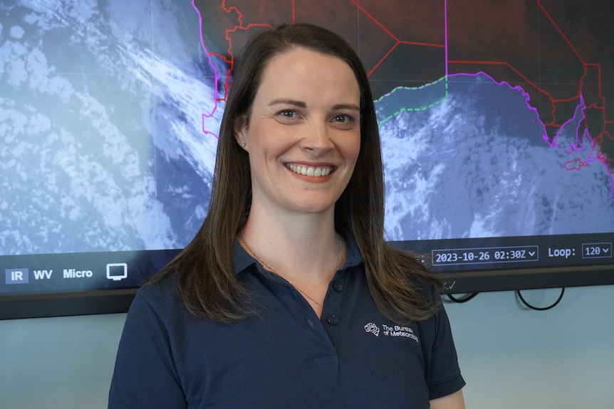 A woman smiling and standing in front of a weather map