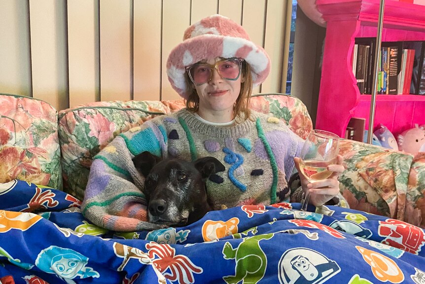 Alex and Ziggy under a blanket on the couch as Alex wears a fuzzy hat