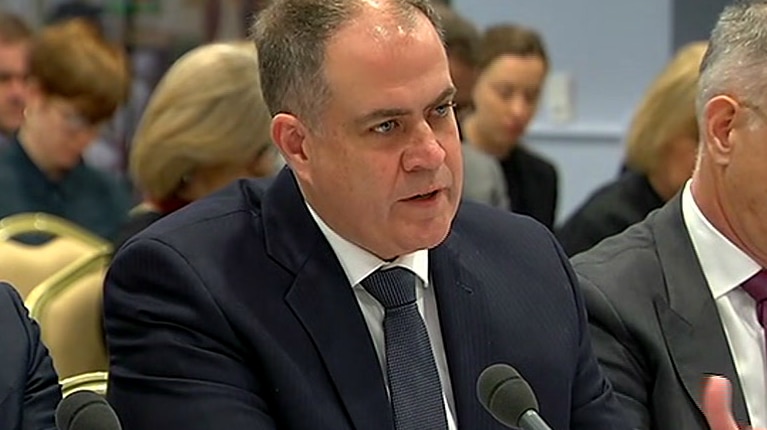 A man in a suit sits in front of a microphone.