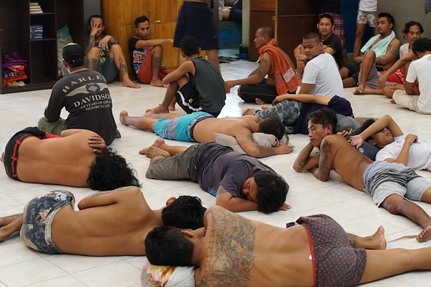 Men, many with tattoos on their arms, legs and backs, lie on the ground inside the Kerobokan prison.