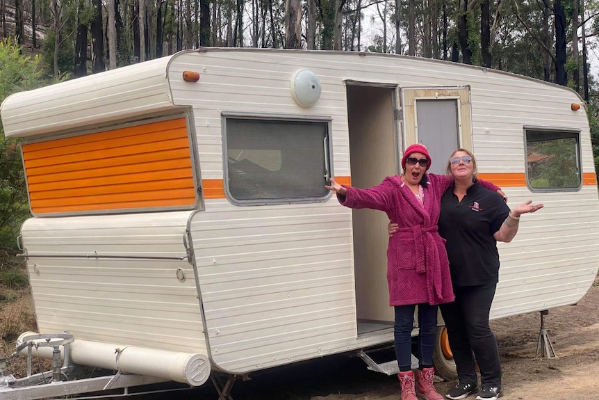 Two women looking excited outside of a caravan.