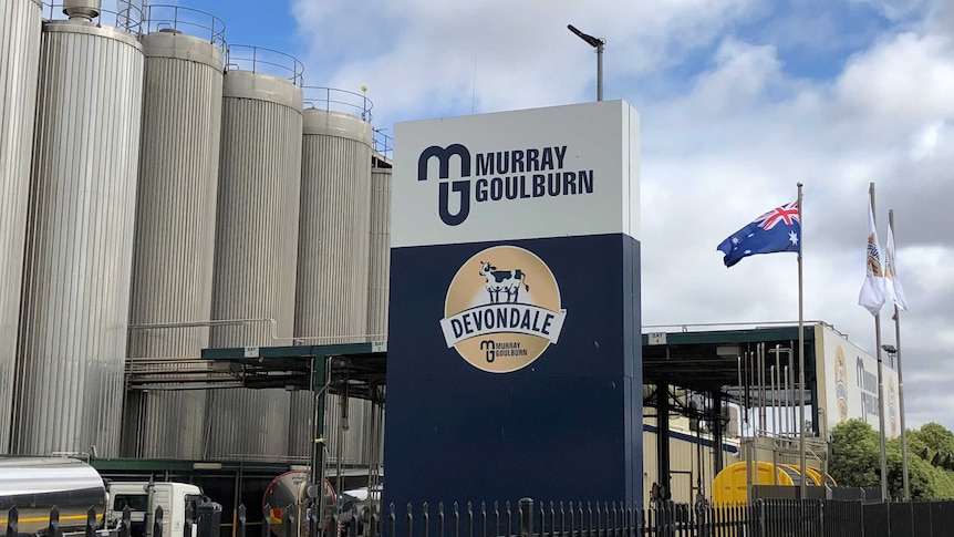 A dairy factory showing metal silos in the background, with a sign in the foreground showing the Devondale Murray Goulburn logos