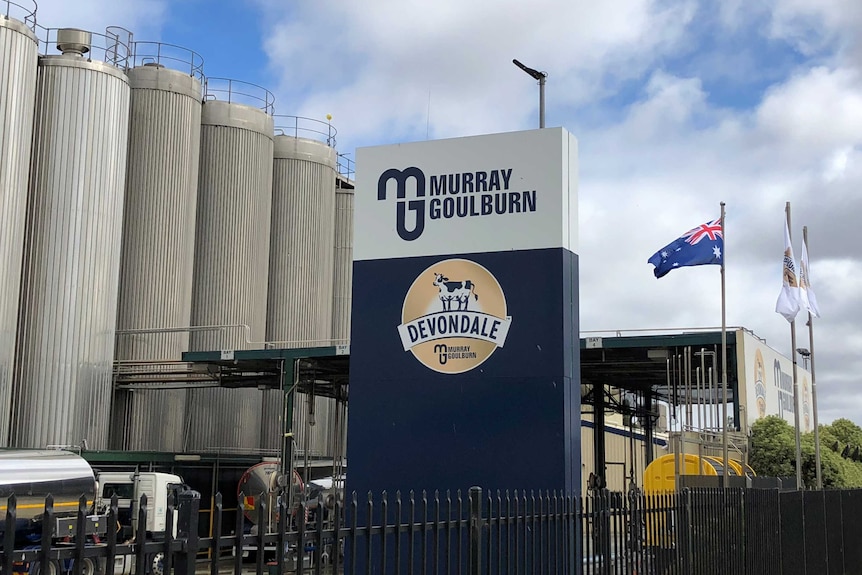 A dairy factory showing metal silos in the background, with a sign in the foreground showing the Devondale Murray Goulburn logos
