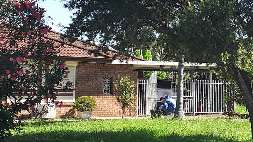 A forensics police officer dressed in a blue jumpsuit works outside a brick house in Bonnyrigg.
