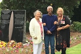 Two Indigenous Elders (women) stand with an Indigenous man in front of a war memorial