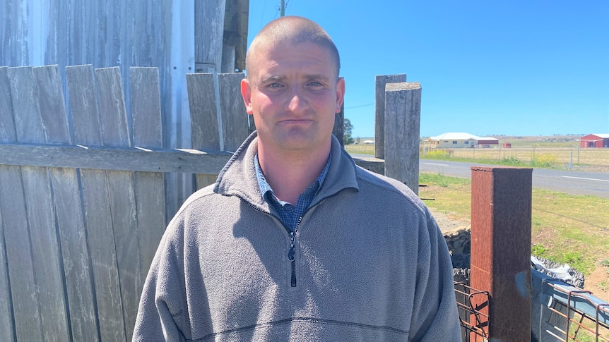 A bald man in a grey sweater standing outside