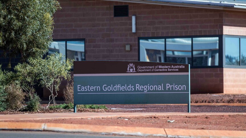 A sign that reads "Eastern Goldfields Regional Prison" outside a squat brick building.