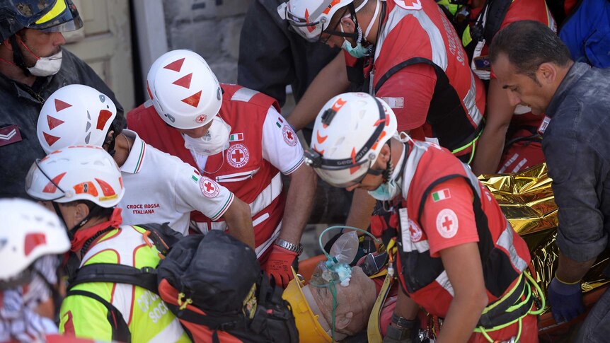 Rescue and emergency services personnel carry away a survivor on a stretcher during search and rescue operation