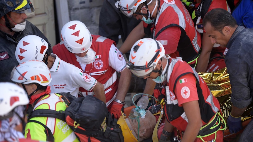 Rescue and emergency services personnel carry away a survivor on a stretcher during search and rescue operation