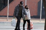A couple wearing masks hold hands as they cross an empty road.
