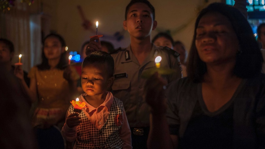 Indonesian tsunami survivors hold a candlelight vigil, with a toddler looking at a flickering flame in a flower-shaped holder.