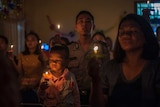 Indonesian tsunami survivors hold a candlelight vigil, with a toddler looking at a flickering flame in a flower-shaped holder.