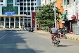 Lone man rides a motorbike on an empty city street in Mandalay.