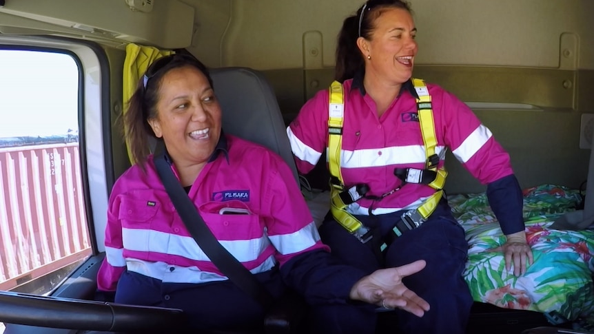 Two women in high-vis pink jackets laugh inside a truck.