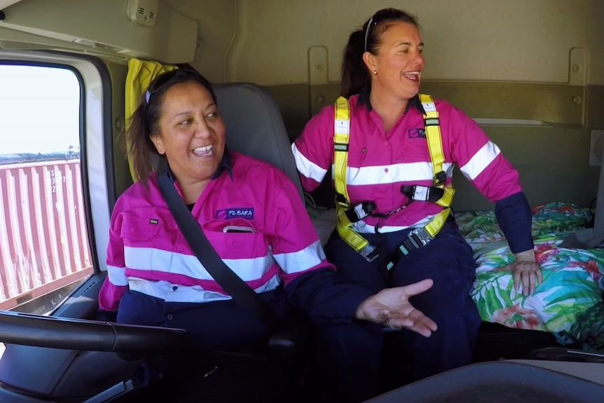 Two women in high-vis pink jackets laugh inside a truck.