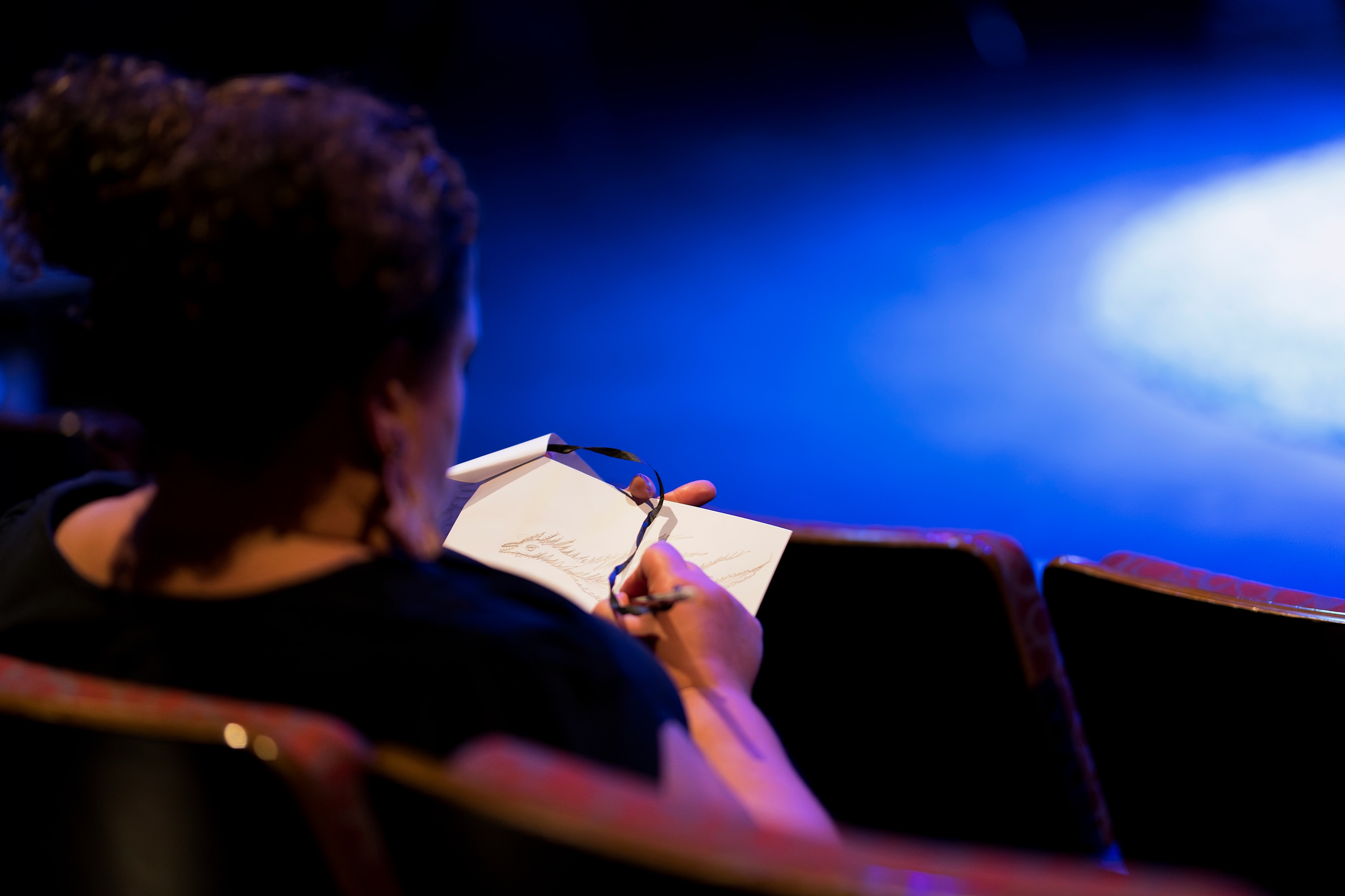 Woman in theatre seat with paper and pencil drawing a dragon