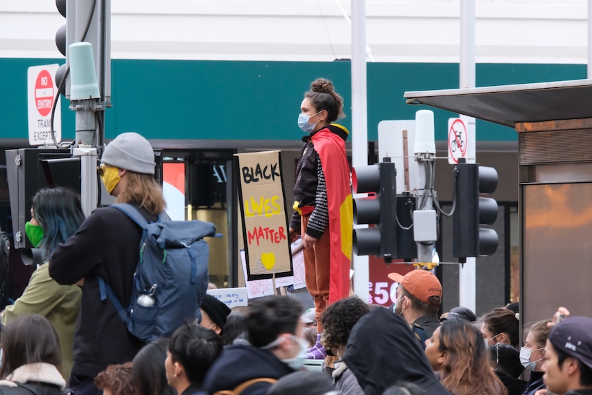 A child stands on top of a structure wearing an Aboriginal flag and a face mask during a protest.