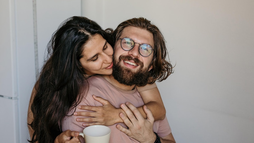 Woman wraps her arms around man and kisses his cheek in a story about setting boundaries in the bedroom.