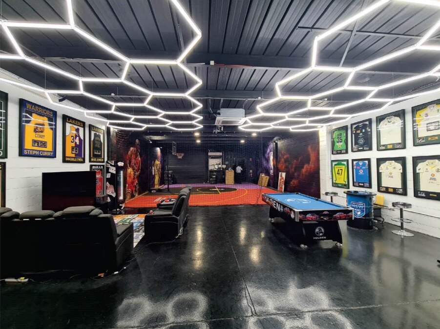 An open plan office with hexagonal LED lights on the ceiling, framed sports jerseys, couches and a basketball court.