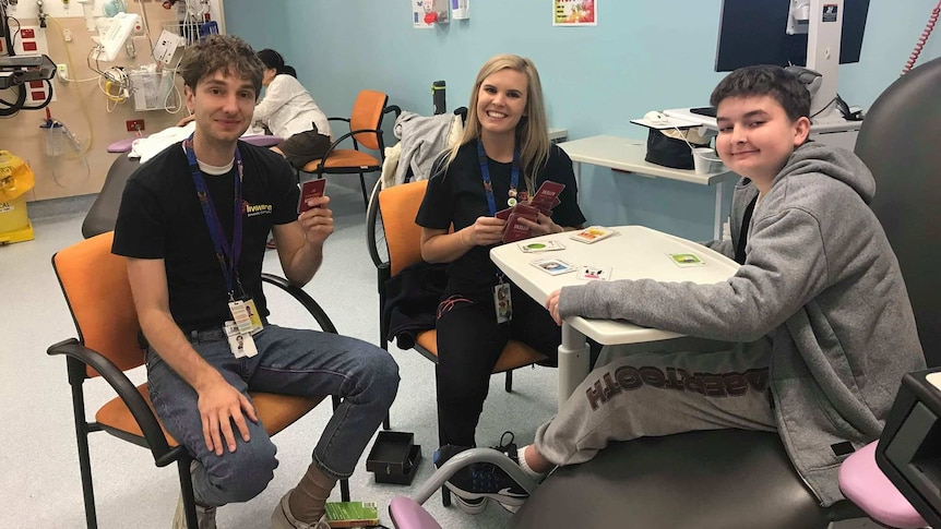 Two men and a woman play cards in a hospital ward