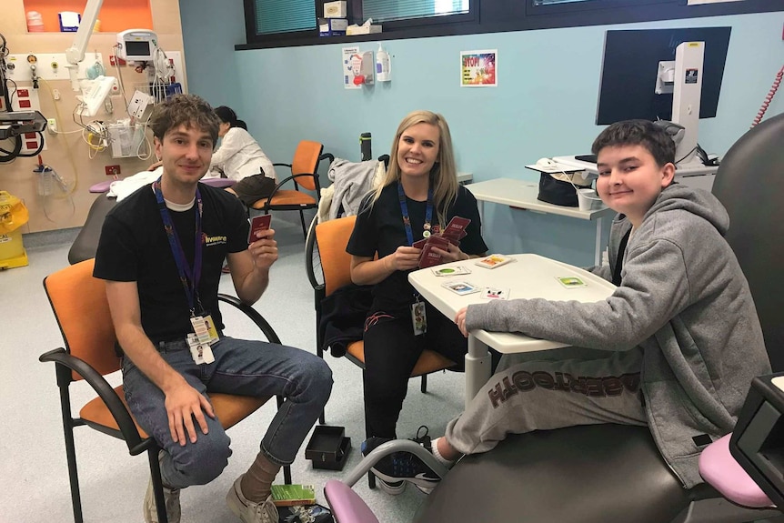 Two men and a woman play cards in a hospital ward