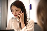 An Asian woman speaking on a phone.