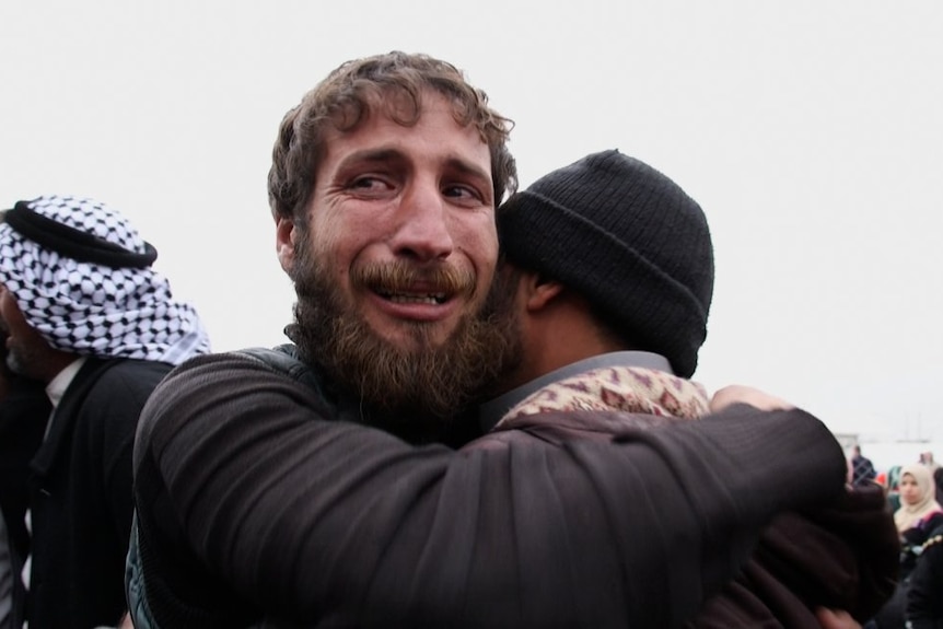 Two men, one with tears in his eyes, hug in the Hammam Al Alil camp south of Mosul.