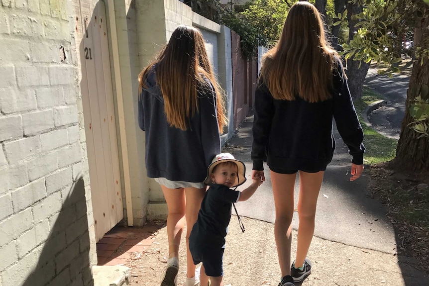 Two young teenage girls walking along a footpath holding hands with a toddler