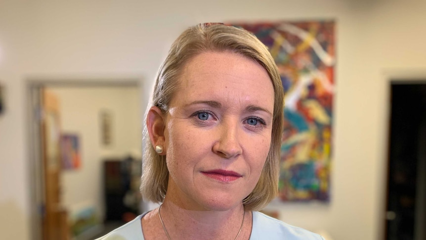 A woman in a blue blouse looking straight into the camera, standing in an office