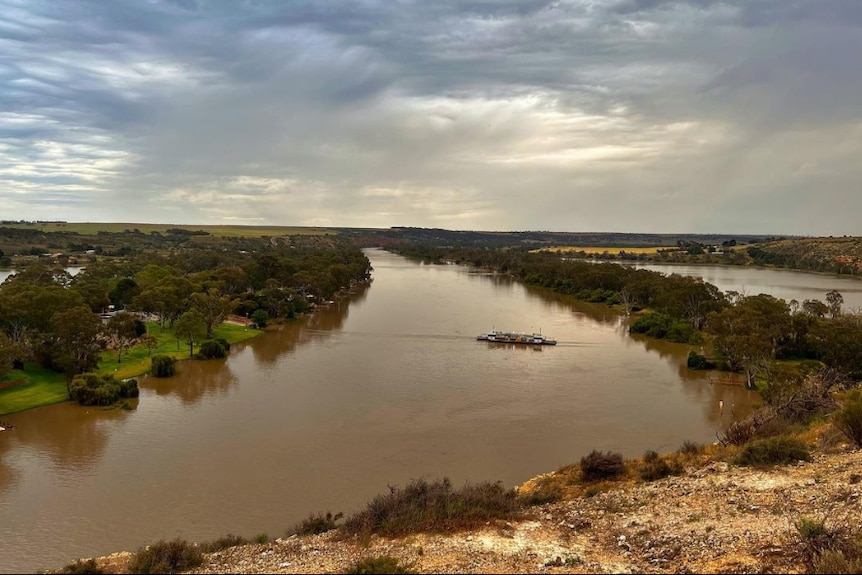 A wide bend in the river with cliffs on one side and green trees and land on the other.