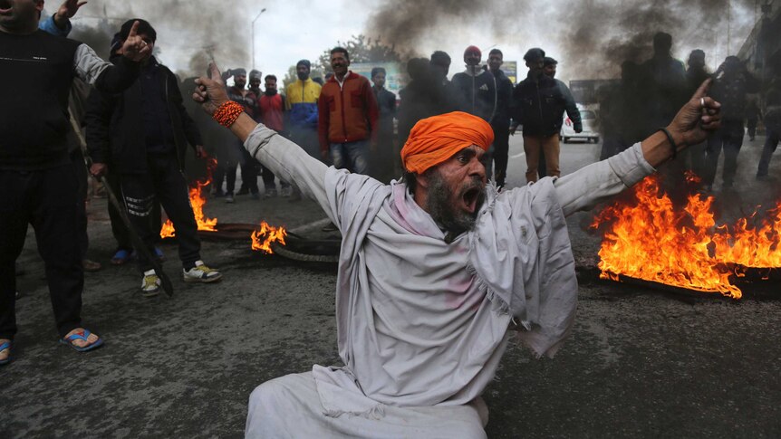A protestor shouts slogans as fire burns and smoke rises in the background.
