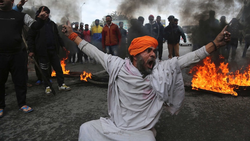 A protestor shouts slogans as fire burns and smoke rises in the background.