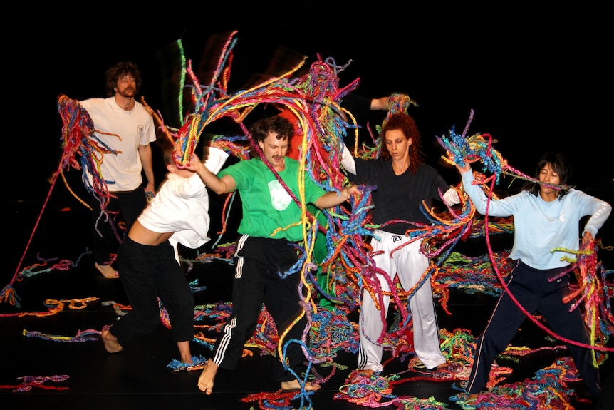 Um grupo de dançarinos joga lã colorida no palco