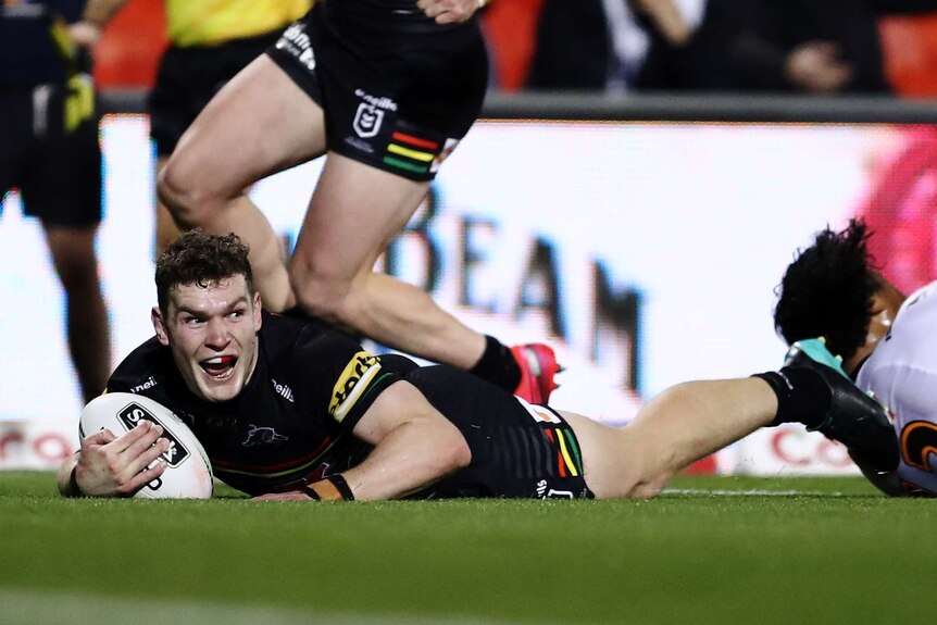 A Penrith Panthers NRL player lies on the ground holding the ball in his right arm after scoring a try.