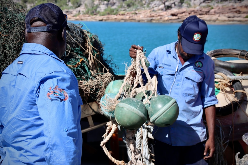 Rangers holding ghost nets with the sea in the background.