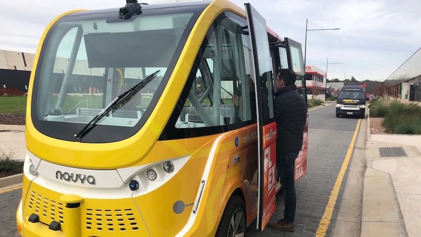 Man stands at open doors of an autonomous shuttle bus is launched at Flinders University in Adelaide.