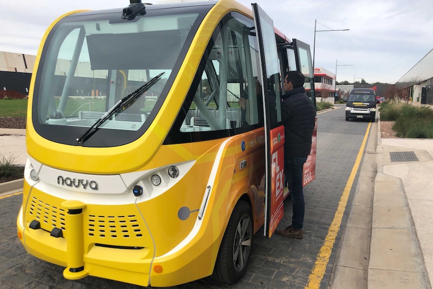 Man stands at open doors of an autonomous shuttle bus is launched at Flinders University in Adelaide.