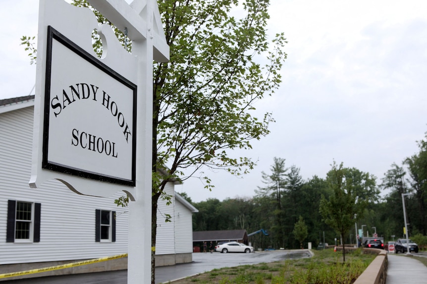 A decorative white sign on the corner of a driveway reads "Sandy Hook School"