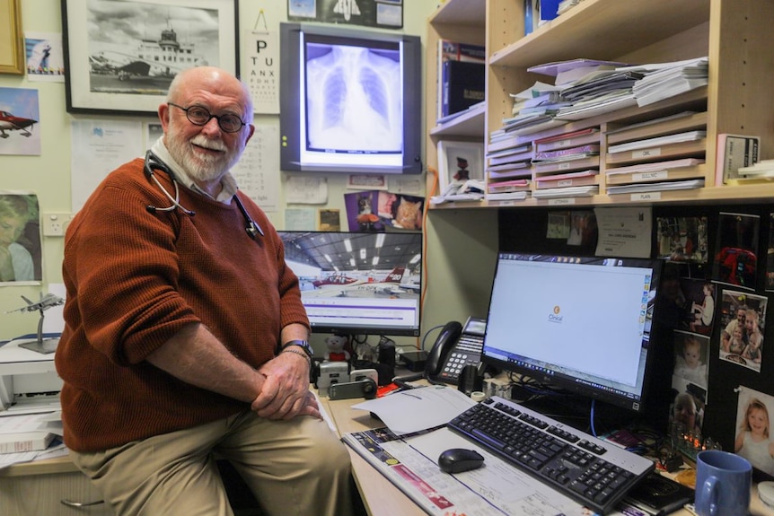 Chris sits on his desk with papers and xrays around him.